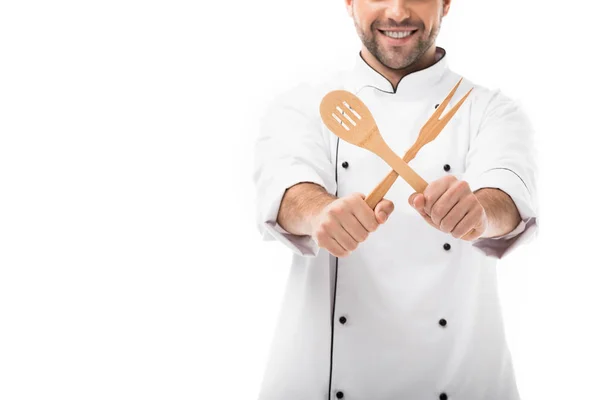 Tiro recortado de sorrindo jovem chef segurando utensílios de cozinha de madeira isolados em branco — Fotografia de Stock