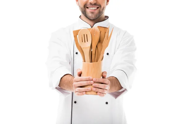 Recortado disparo de sonriente joven chef con montón de utensilios de cocina de madera aislados en blanco - foto de stock