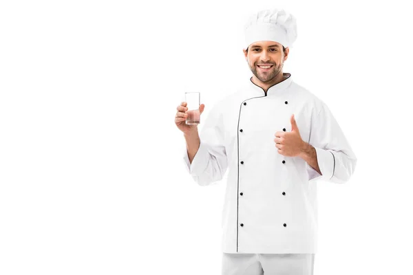 Sonriente joven chef con vaso de agua mostrando el pulgar hacia arriba aislado en blanco - foto de stock