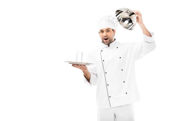 Sorprendido joven chef apertura seving domo con vaso de agua en el interior aislado en blanco - foto de stock