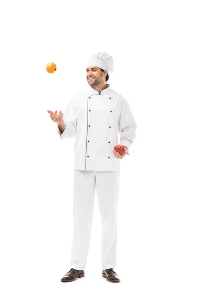 Heureux jeune chef jonglant avec tomate et poivron isolé sur blanc — Photo de stock