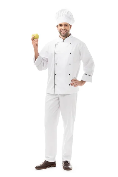 Vista completa de guapo joven chef sosteniendo manzana fresca y sonriendo a la cámara aislada en blanco - foto de stock