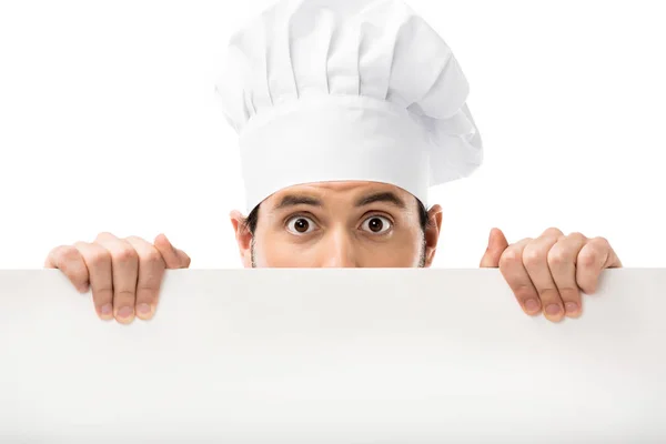 Profissional cozinheiro masculino espiando banner em branco e olhando para a câmera isolada no branco — Fotografia de Stock