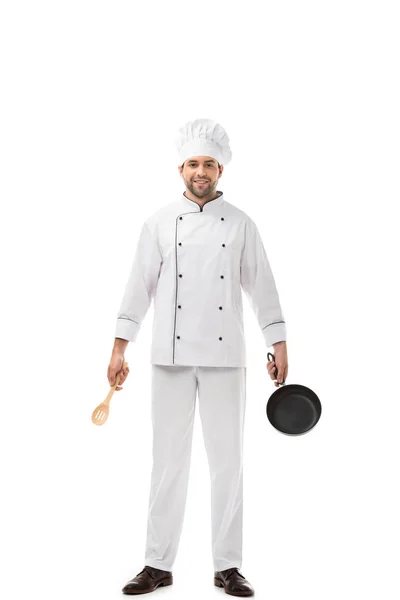 Professional young chef holding utensils above head and smiling at camera isolated on white — Stock Photo