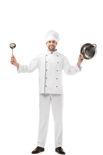 Guapo y sonriente chef sosteniendo cucharón y sartén aislado en blanco - foto de stock