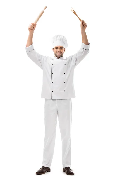 Beau jeune chef tenant des ustensiles au-dessus de la tête et souriant à la caméra isolé sur blanc — Photo de stock