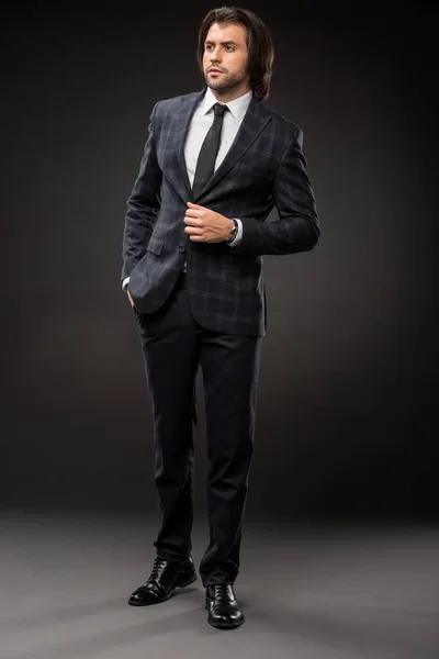 Ganzkörperansicht des professionellen seriösen Geschäftsmannes im eleganten Anzug, der auf schwarz wegschaut — Stockfoto
