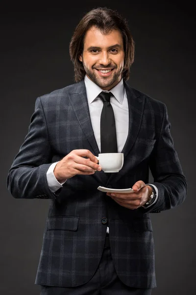 Homem de negócios bonito feliz segurando xícara de café e sorrindo para a câmera isolada em preto — Fotografia de Stock