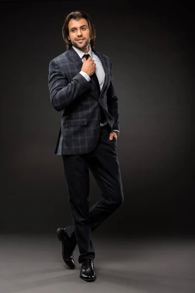 Vista de longitud completa de guapo elegante hombre de negocios ajustando corbata en negro - foto de stock