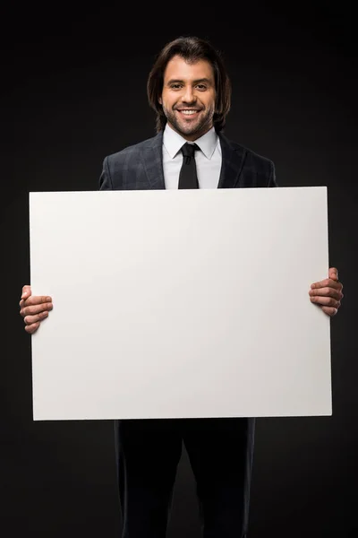 Jovem empresário profissional segurando banner em branco e sorrindo para a câmera isolada em preto — Fotografia de Stock