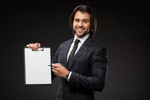 Jovem empresário profissional apontando para a área de transferência em branco e sorrindo para a câmera isolada em preto — Fotografia de Stock