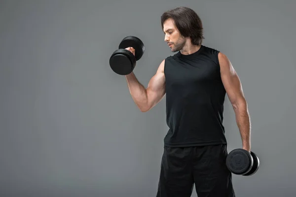 Musculoso joven deportista haciendo ejercicio con mancuernas aisladas en gris - foto de stock