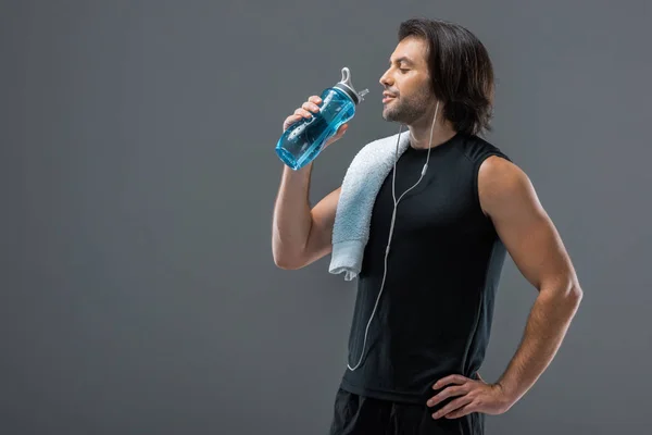 Lächelnder muskulöser Mann mit Handtuch, der Wasser aus Sportflasche trinkt — Stockfoto