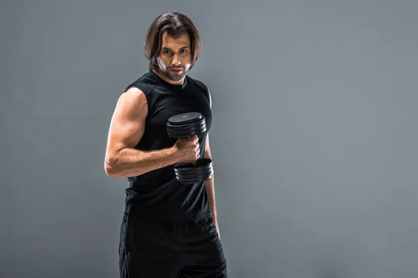 Handsome athletic man holding dumbbell and looking at camera isolated on grey — Stock Photo