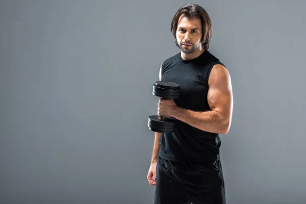 Handsome sport man holding dumbbell and looking at camera isolated on grey — Stock Photo