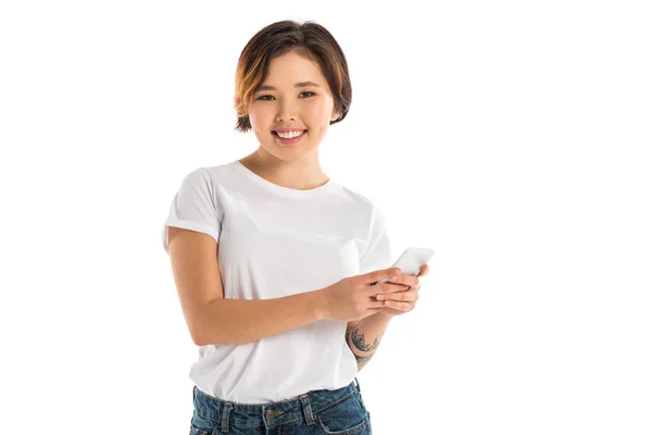 Smiling young woman using smartphone and looking at camera isolated on white — Stock Photo