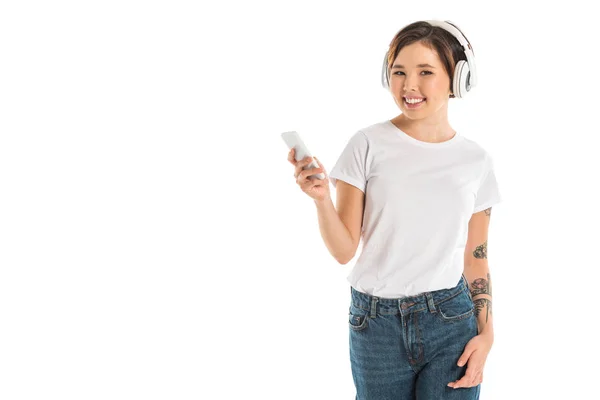 Bela jovem mulher usando fones de ouvido, ouvindo música e usando smartphone isolado no branco — Fotografia de Stock