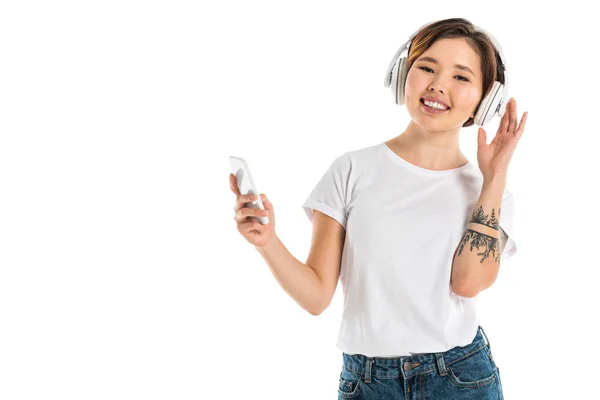 Sorridente giovane donna con le cuffie, ascoltare musica e utilizzando smartphone isolato su bianco — Foto stock