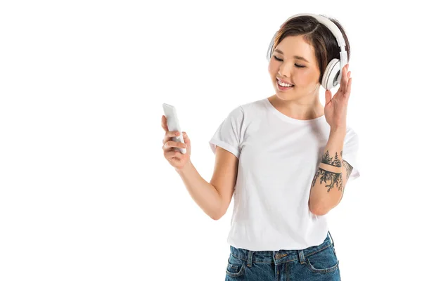 Jovem feliz usando fones de ouvido, ouvindo música e usando smartphone isolado no branco — Fotografia de Stock