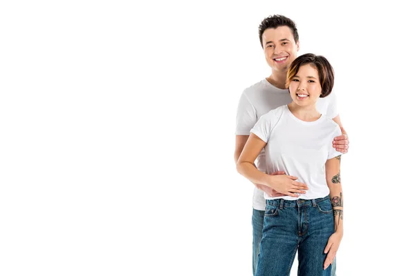 Felice fidanzato guardando la fotocamera e abbracciando sorridente fidanzata isolato su bianco — Foto stock