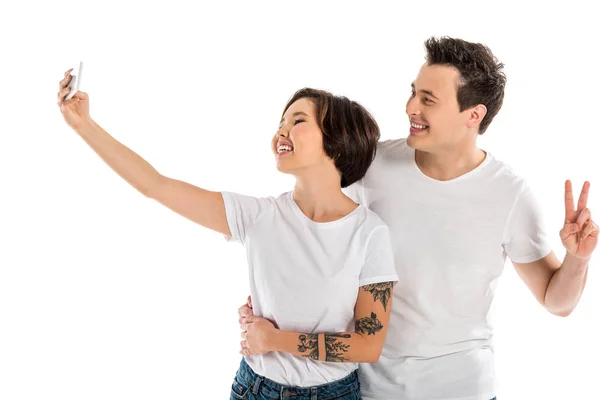 Lächelndes Paar macht Selfie mit Smartphone und zeigt Friedenszeichen auf weißem Grund — Stockfoto