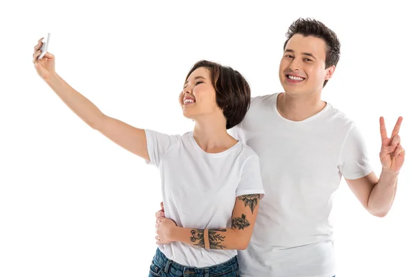 Glückliches Paar macht Selfie auf Smartphone und zeigt Friedenszeichen isoliert auf weißem Grund — Stockfoto