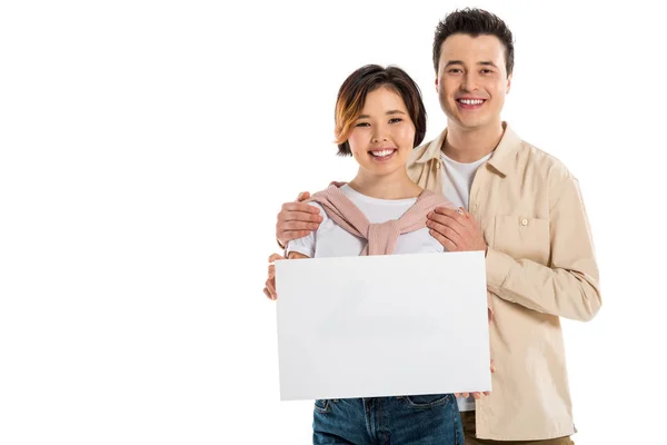 Marido feliz e esposa em roupas casuais olhando para a câmera e segurando placa em branco isolado no branco — Fotografia de Stock