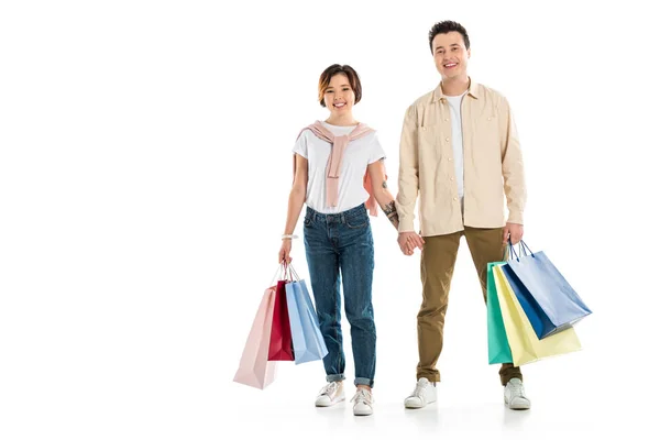 Sorrindo casal olhando para a câmera, de mãos dadas e levando sacos de compras isolados em branco — Fotografia de Stock
