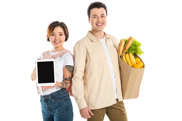 Mari heureux tenant sac d'épicerie tandis que la femme présente tablette numérique avec écran blanc isolé sur blanc — Photo de stock