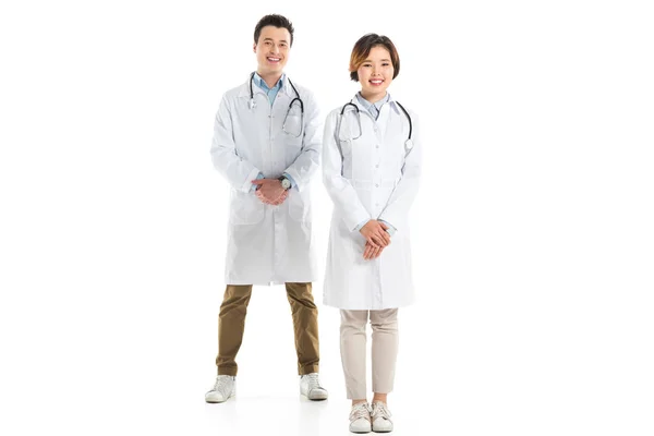 Médicos femeninos y masculinos con las manos dobladas mirando a la cámara aislada en blanco - foto de stock