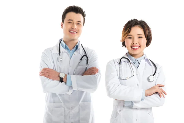 Sonrientes médicos femeninos y masculinos mirando a la cámara con los brazos cruzados aislados en blanco - foto de stock