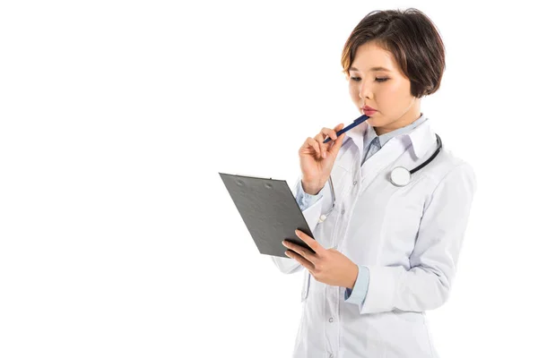 Médico femenino pensativo que sostiene el diagnóstico y la pluma aislados en blanco - foto de stock