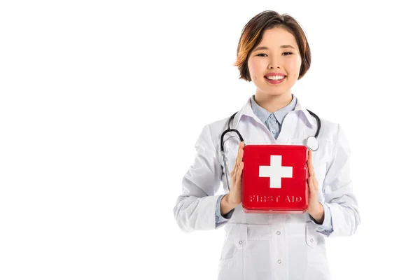 Sonriente médico femenino aislado en blanco celebración botiquín de primeros auxilios y mirando a la cámara - foto de stock