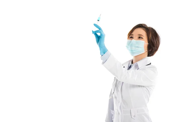 Médico femenino serio con mascarilla médica sosteniendo la jeringa y mirando hacia arriba aislado en blanco — Stock Photo