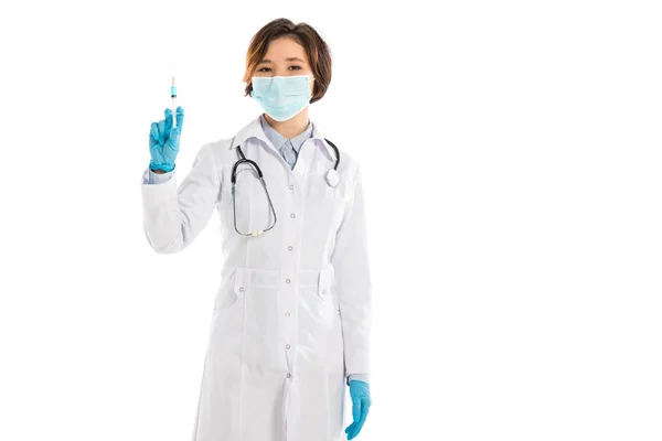 Médico fêmea em máscara médica segurando seringa e olhando para a câmera isolada no branco — Fotografia de Stock