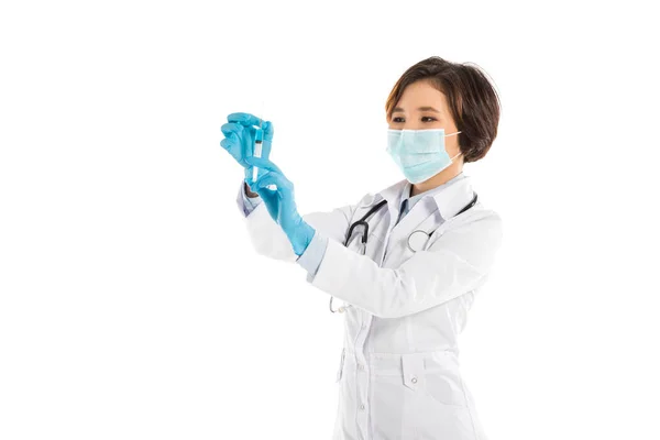 Médico fêmea concentrado em máscara médica segurando seringa isolada em branco — Fotografia de Stock