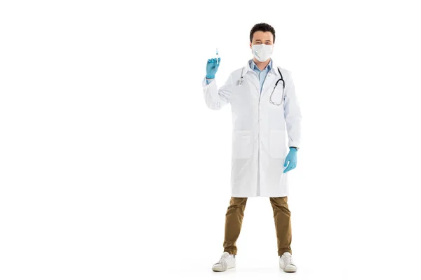 Médico do sexo masculino em máscara médica em pé e segurando seringa isolada em branco — Fotografia de Stock