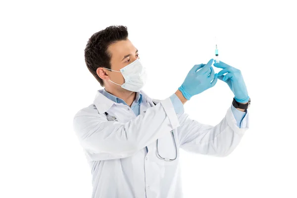 Концентрированный врач-мужчина в резиновых перчатках и маске, держащий шприц, изолированный на белом — стоковое фото