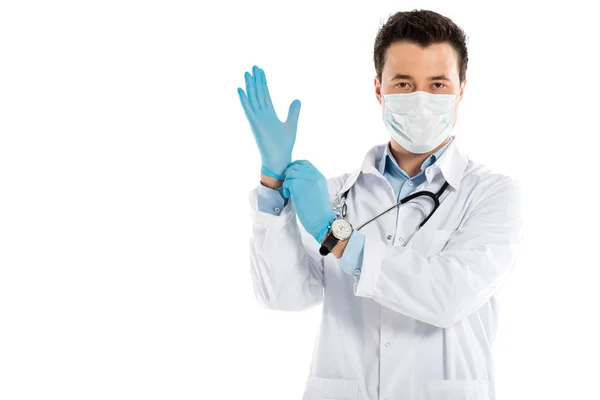 Schöner männlicher Arzt zieht Gummihandschuhe an und schaut isoliert auf weiße Kamera — Stockfoto