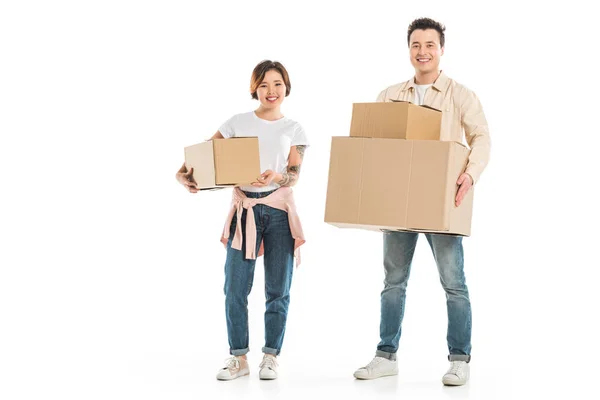 Feliz pareja mirando a la cámara y sosteniendo cajas de cartón aisladas en blanco, moviéndose a nuevo concepto de casa - foto de stock