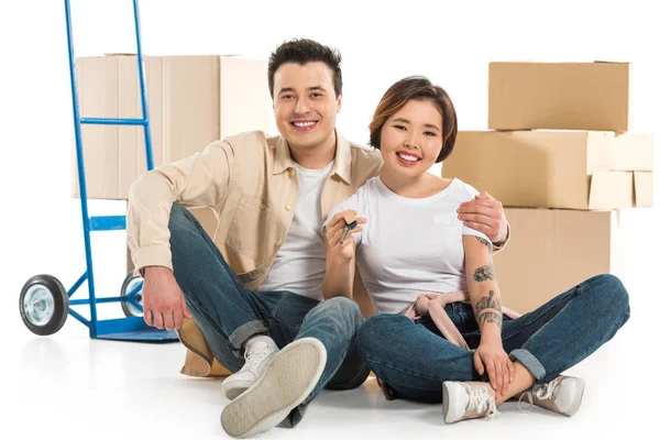 Couple hugging and holding keys with cardboard boxes on background, moving to new house concept — Stock Photo