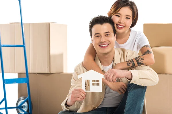 Couple hugging and holding house model with cardboard boxes on background, moving to new house concept — Stock Photo