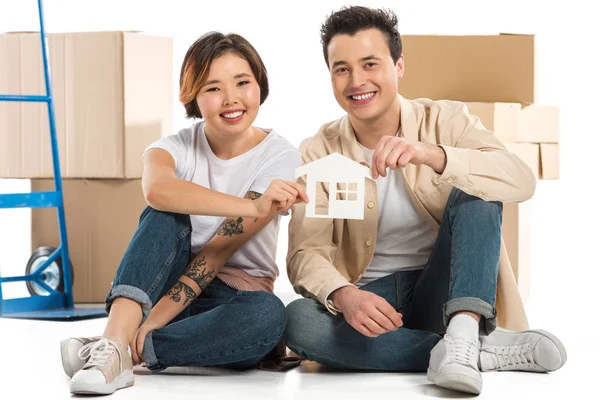 Чоловік і дружина тримають модель будинку з картонними коробками на фоні, переходячи до нової концепції будинку — стокове фото