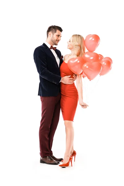 Hermosa pareja sonriente abrazándose mientras sostiene globos rojos aislados en blanco - foto de stock