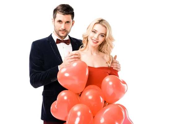 Casal feliz olhando para a câmera enquanto segurando balões vermelhos isolados no branco — Stock Photo