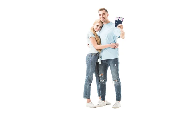 Hombre sosteniendo pasaportes con boletos y abrazando a mujer aislada en blanco - foto de stock