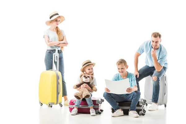 Familia feliz sentada en el equipaje y mirando en el mapa aislado en blanco - foto de stock