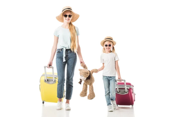 Madre e hija sosteniendo osito de peluche y equipaje aislado en blanco - foto de stock