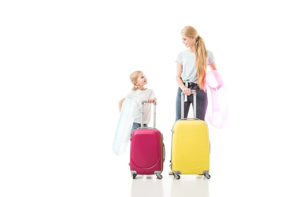 Madre e hija sonriendo y sosteniendo el equipaje aislado en blanco - foto de stock