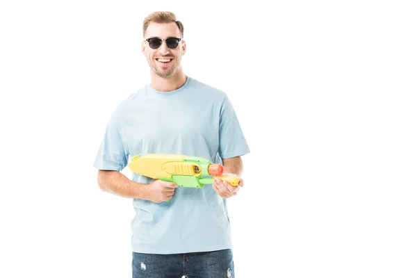 Homme joyeux tenant pistolet à eau et debout dans des lunettes de soleil isolées sur blanc — Photo de stock